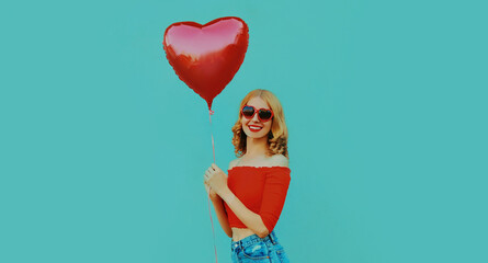 Portrait of cute smiling woman with red heart shaped balloon on a blue background
