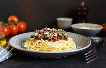 Spaghetti with bolognese sauce, basil and parmesan on a dark concrete background.