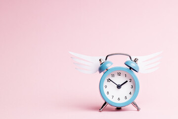 blue alarm clock with origami wing over pink pastel background. valentine romance day concept....