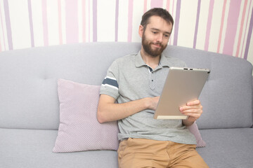 Attractive young man is using a tablet and smiling on sofa at home