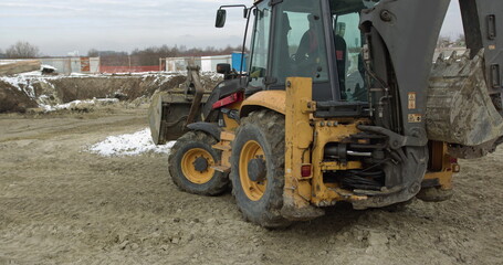 Fototapeta na wymiar Construction Machinery At Work On Building A House. Different Types Of Tractors And Excavators Prepare The Soil For Plant Construction In The Industrial Zone. Bulldozer Rides on Sandy Road