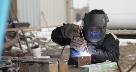 Close-up blacksmith welder in protective mask works with metal using a welding machine, bright sparks.