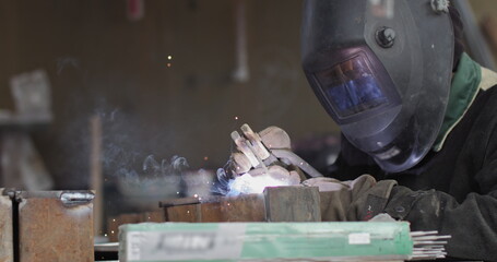 Close-up blacksmith welder in protective mask works with metal steel and iron using a welding machine, bright sparks and flashes in extreme slow motion