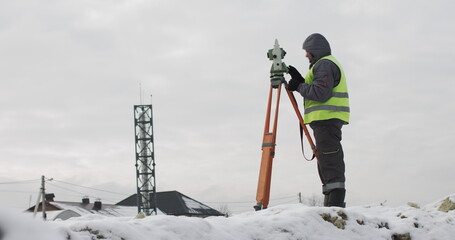 Construction engineer supervising work at building site. Professional engineer surveyor takes measures with theodolite. Worker using a theodolite geodetic optical device on a construction site