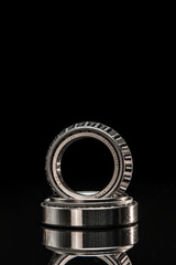 Car bearings, auto parts, steel automotive bearings, placed on black reflective surface, on black background.
