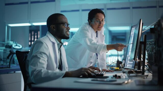 Electronics Research, Development Facility: Engineer Project Manager Talks With Scientist working on Computer. Diverse Team of Professionals Design Silicon Microchip, Semiconductors, Motherboard 