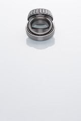 Car bearings, auto parts, steel automotive bearings placed on white reflective surface on top of the frame with negative space. 