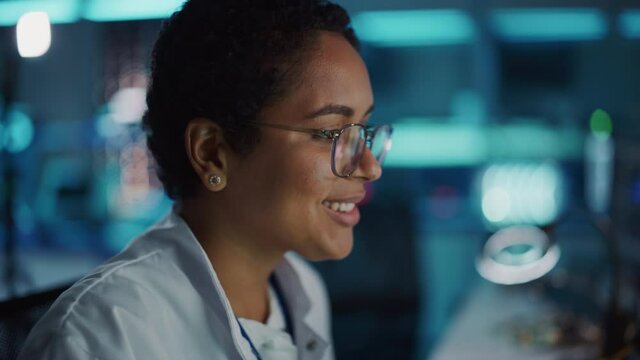 Portrait of Beautiful Black Latin Woman Computer Screen Reflecting in Her Glasses. Young Intelligent Female Scientist Working in Laboratory. Background Bokeh Blue with High-Tech Technological Lights