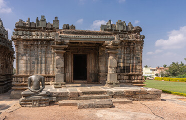 Lakkundi, Karnataka, India - November 6, 2013: Brahma Jinalaya temple. Separate sanctuary on side of main temple under blue cloudscape in green park. Jain statue in front.