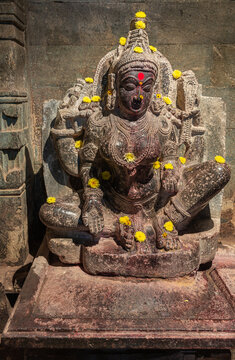 Lakkundi, Karnataka, India - November 6, 2013: Brahma Jinalaya temple. Closeup of damaged black stone statue of padmavati. Yellow flowers dispersed on top.
