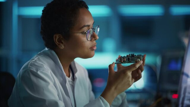 Modern Electronics Research and Development Facility: Beautiful Black Female Engineer Inspects Printed Circuit Board Motherboard. Scientist Designs Industrial PCB, Silicon Microchips, Semiconductors