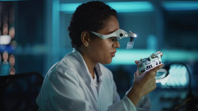 Modern Electronics Research and Development Facility: Beautiful Black Female Engineer Inspects Printed Circuit Board Motherboard. Scientist Designs Industrial PCB, Silicon Microchips, Semiconductors