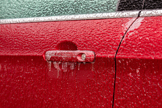 Closeup of car door handle and lock covered in ice during winter storm. Concept of winter driving preparedness and safety