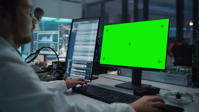 Modern Electronics Facility: Scientist, Engineer Works on Green Chroma Key Screen Computer. Design, Development of Industrial PCB, Silicon Microchips, Semiconductors, Telecommunications Equipment