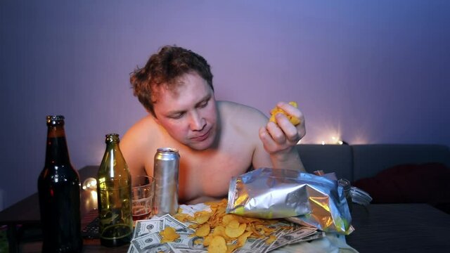 Boor man with a naked torso eats chips and drinks beer