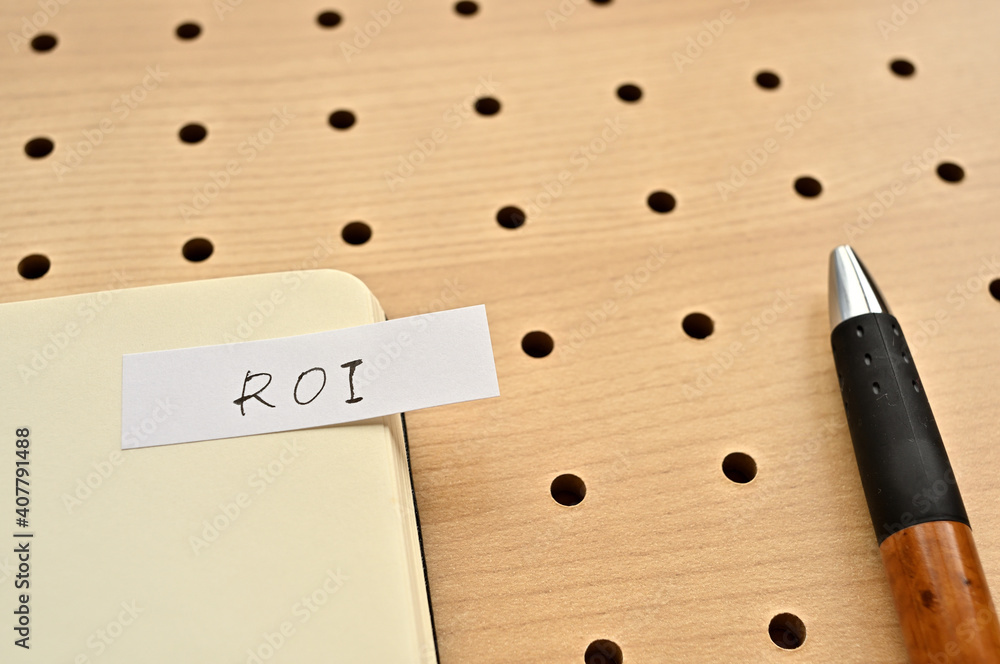 Poster a sticky note with roi written on the edge of an open notebook on the punching board. that's an acro