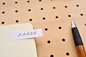 A sticky note with AARRR written on the edge of an open notebook on the punching board. That's an...