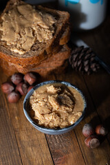 Homemade nut butter in a small bowl. Slices of bread with homemade hazelnut spread and glass of milk on wooden table.  Homemade Hazelnut Butter. 