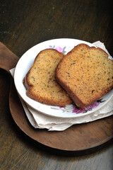 Two slices of banana bread on a small plate with a wooden chopping board