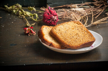 two slices of banana bread on a small plate with a wooden chopping board and garnish with flowers and straw
