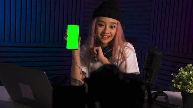 Zoomer asian girl talking about smartphone or application. Chromakey on the screen of device. UGC. Bloggers studio with microphone. Recording amera in front of the girl