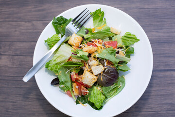 Salad of romaine lettuce, croutons, shredded cheddar cheese, and tomato on a white plate on a wooden table
