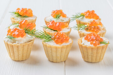 Tartlets with caviar and cream cheese on a white wooden table.