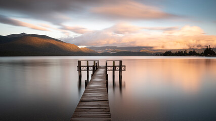 Fototapeta na wymiar Long exposure image of lake Te Anau jetty at sunrise with a spectacular backdrop of Mt Luxmore and the Murchison mountains