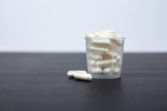 transparent shot glass filled with medicine pills on white black background, side view