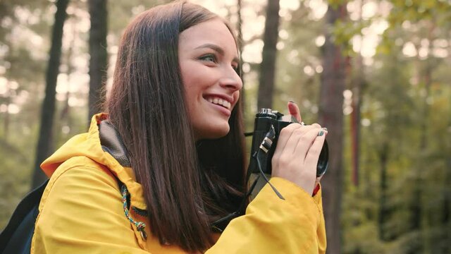 Close up of young beautiful girl in yellow jacket makes photo of nature on her camera standing in woods. Hobby photographer concept.