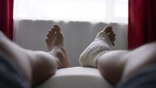 Male bending and exercising his toes as he lays with an injured ankle in bandages