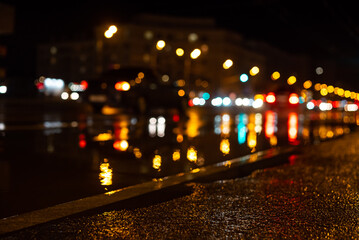 Blurred focus of a central city road during the rain at night, with colorful unfocused lights in the background. Water from the rain and the reflection of lanterns in the city
