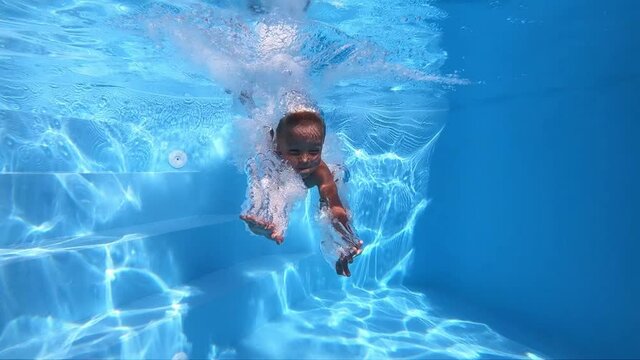 The child is floating under water.
A young boy swims underwater in a clean pool. Underwater shot. Slow motion.