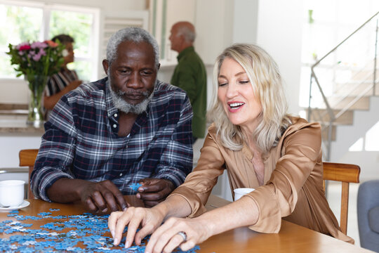 Senior caucasian woman and african american man sitting by table doing puzzles at home