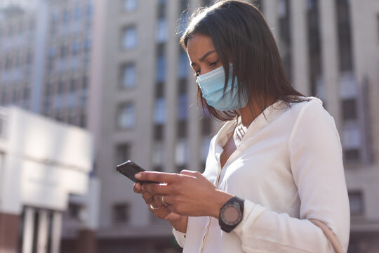 African american woman wearing face mask using smartphone on the street