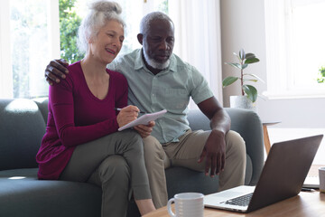 Senior mixed race couple using laptop paying bills together in living room