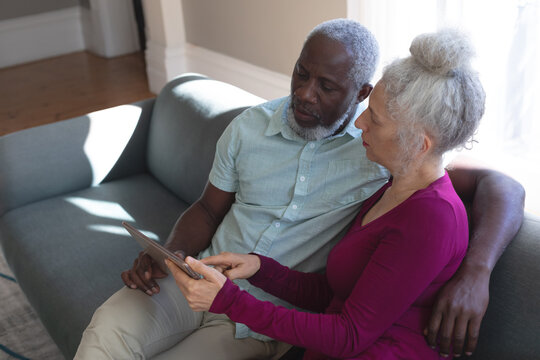 Senior mixed race couple sitting on couch looking at digital tablet together in living room