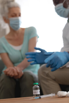 Senior african american male doctor preparing covid 19 vaccination for senior caucasian woman at hom