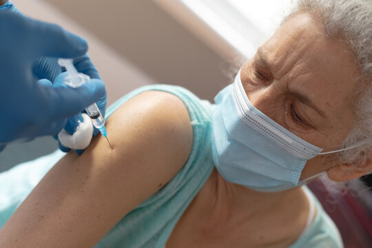 Doctor Wearing Surgical Gloves Giving Senior Female Woman Covid 19 Vaccination At Home