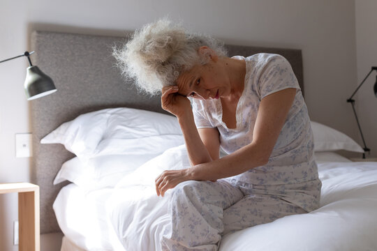 Senior caucasian woman feeling weak sitting on bed