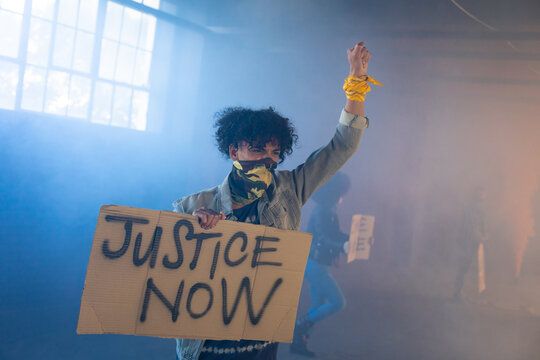 Mixed race man wearing face mask holding protest sign raising fist