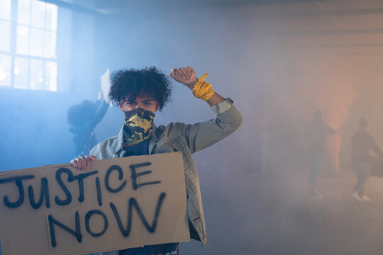 Mixed race man wearing face mask holding protest sign raising fist