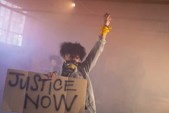 Mixed race man wearing face mask holding protest sign raising fist