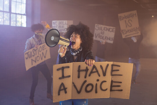 Mixed race woman shouting in megaphone holding protest sign