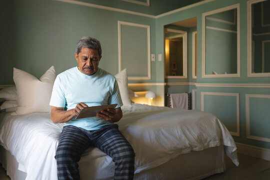 Senior african american man sitting on a bed using digital tablet in a sleeping room