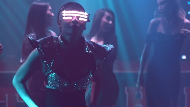 Group of people dance in disco night club to the beat of music from DJ on stage . New year night party and nightlife concept .