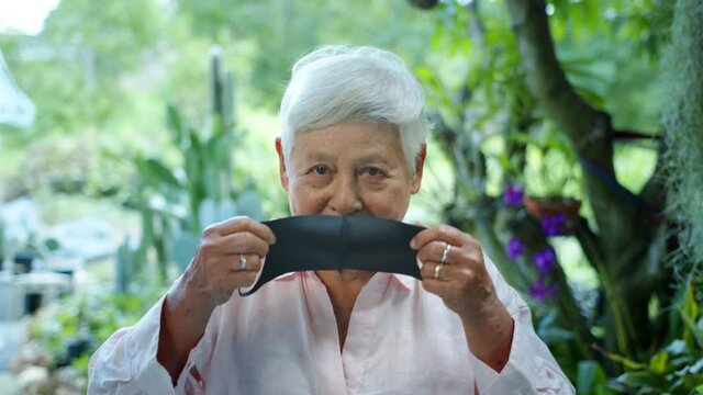 Medium Shot, slow motion of Happy Pretty Asian senior woman with white hair putting a protective face mask on her face. COVID-19 Prevention for the elderly.