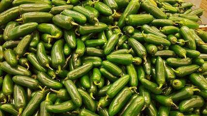 Green fresh Green Jalapeno chili peppers loosely stacked in a traditional vegetable market ready for sale. Raw spicy food ingredients.