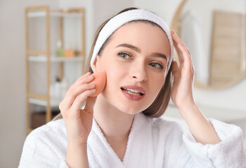 Beautiful young woman with sponge applying makeup at home