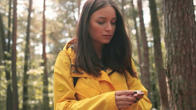 Close up of young beautiful caucasian girl in yellow jacket lost in woods and looking for way using compass.